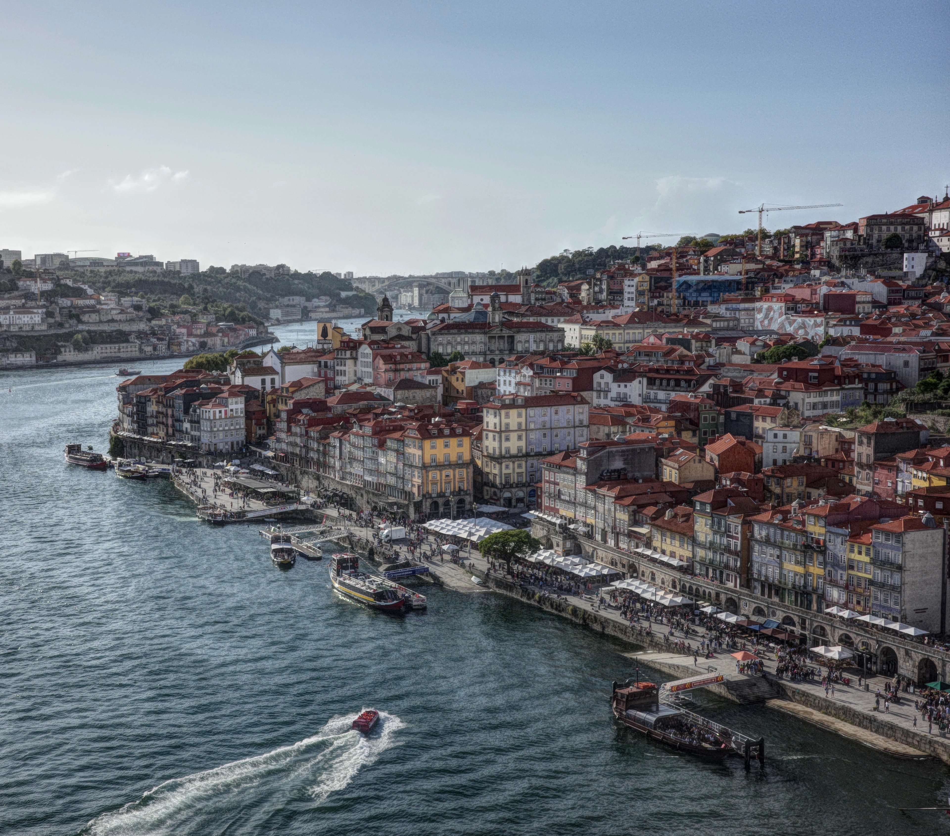 Colorful buildings line the Douro River as a boat leaves a foamy wake.