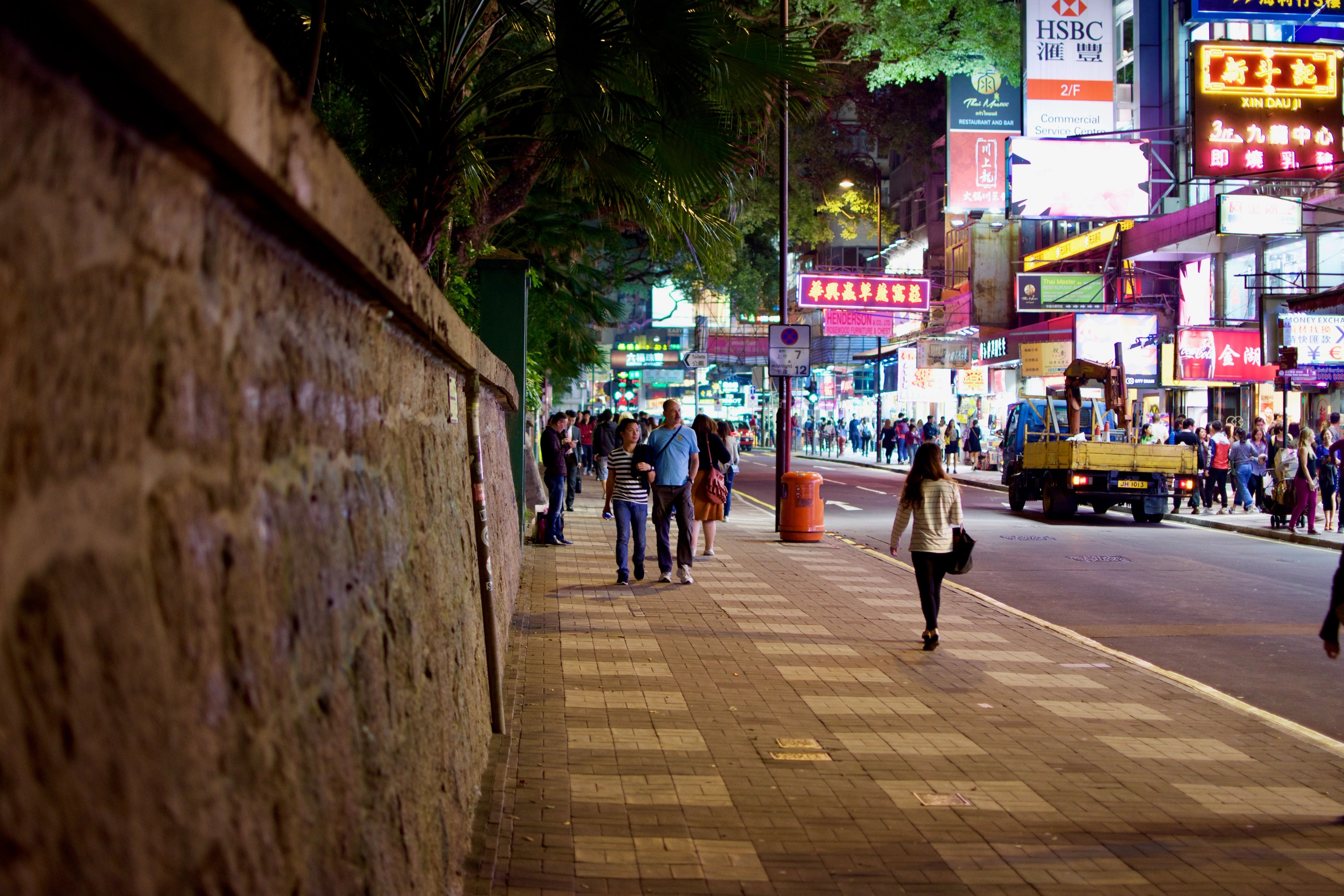 Pedestrians walk along a busy, brightly lit commercial street at night.