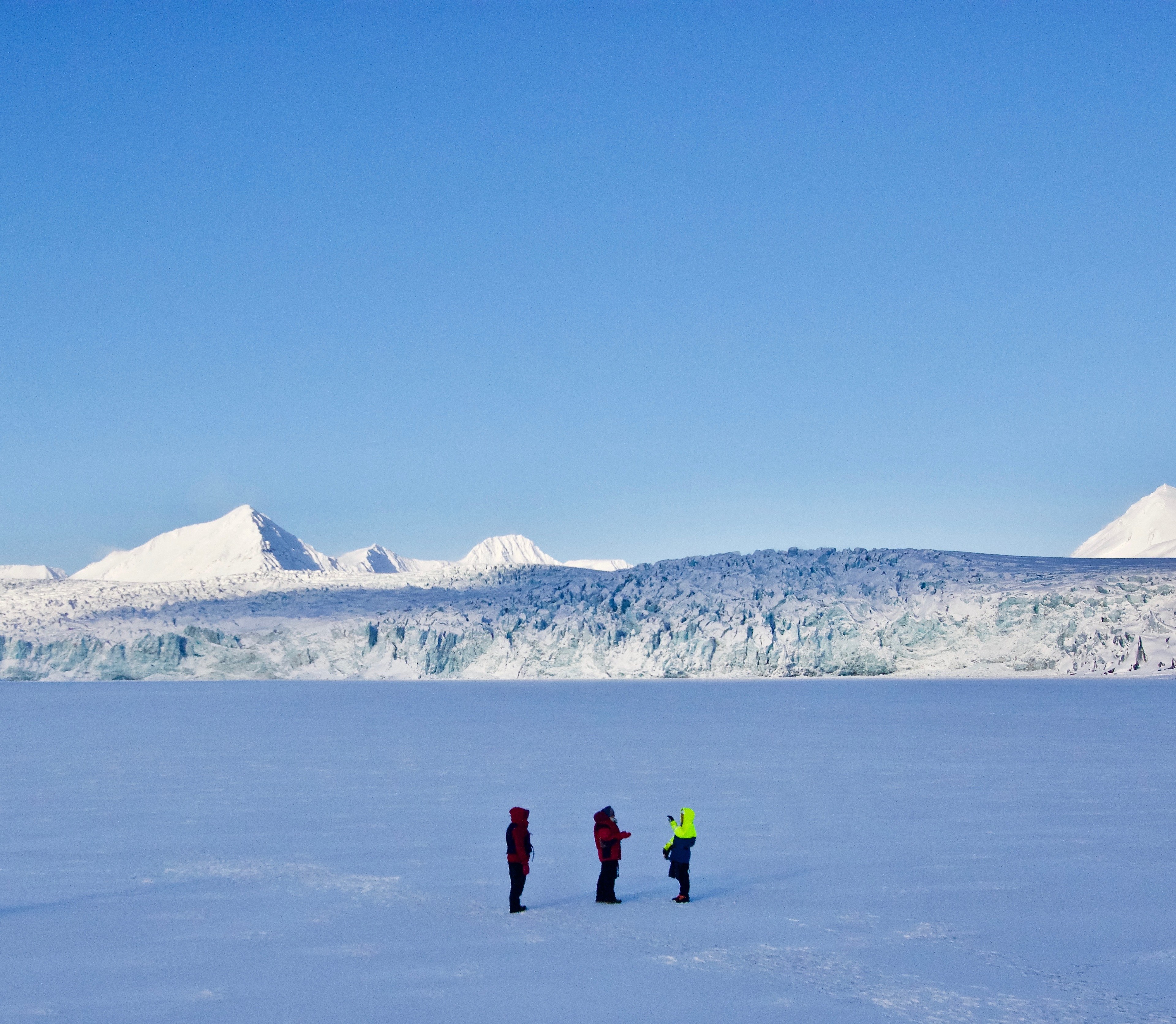 Three small figures cross a wide plain beneath snowy peaks.