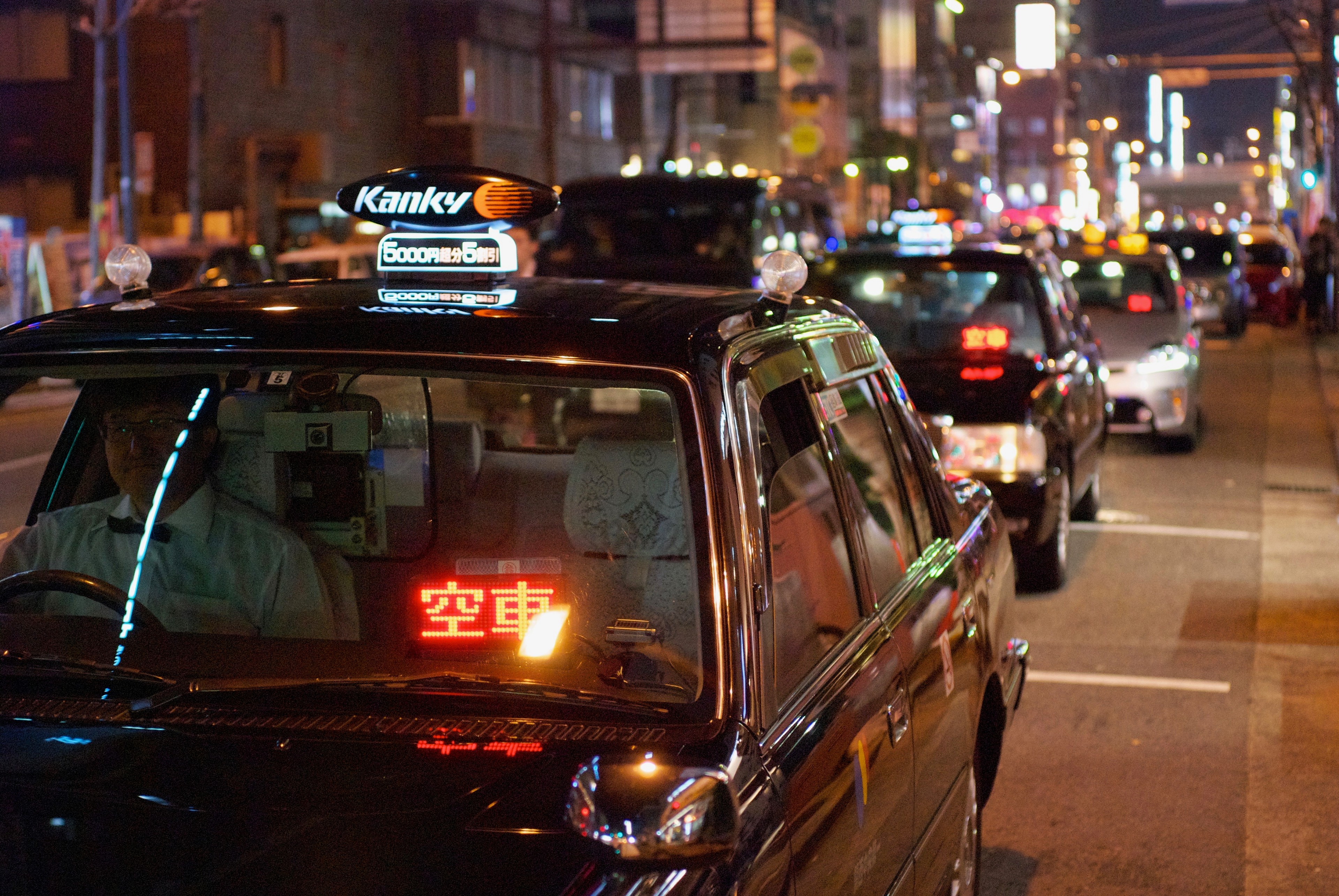 Several yellow taxis travel through a crowded city street at night.