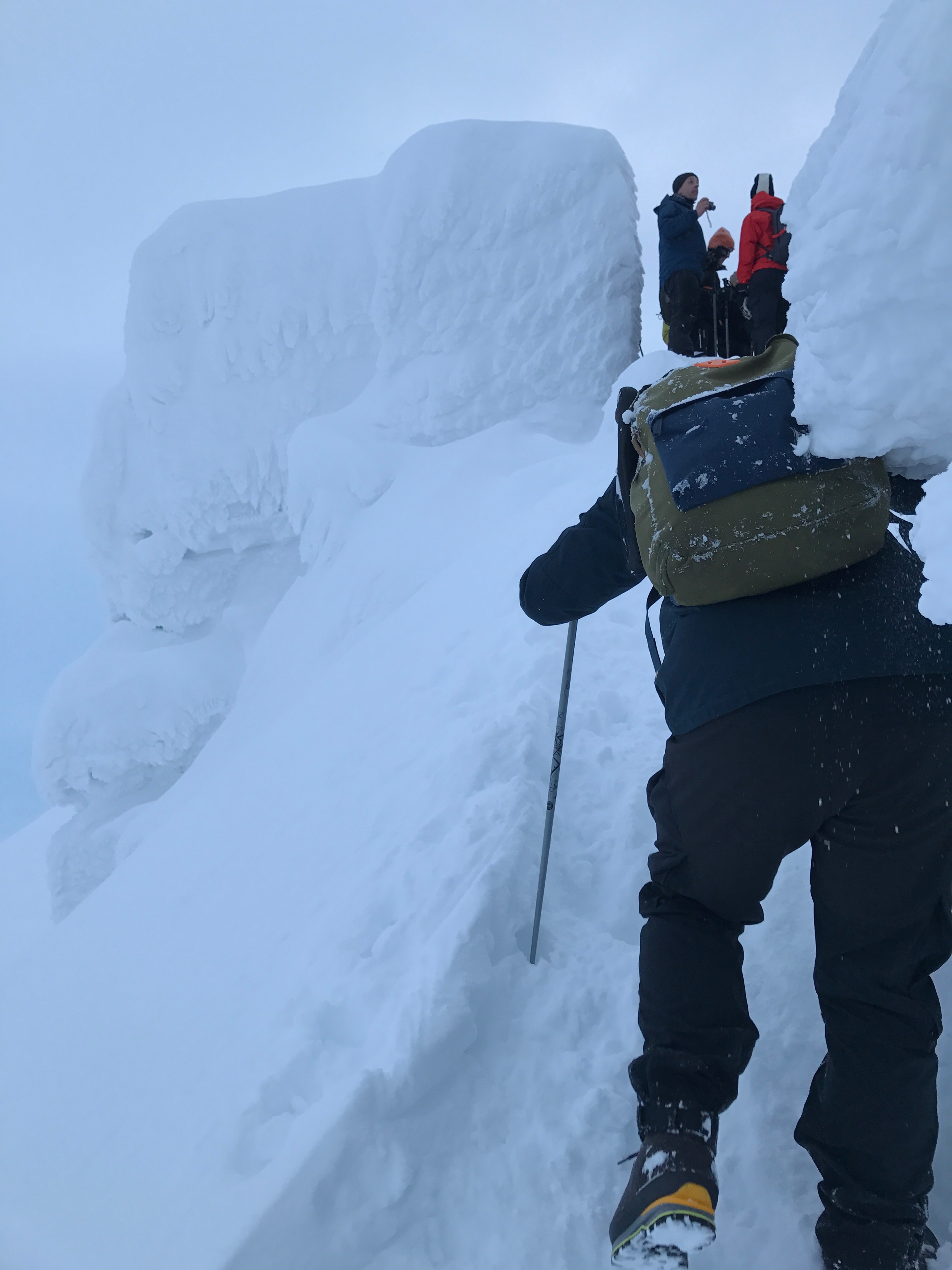 A hiker looks toward a steep snow wall.