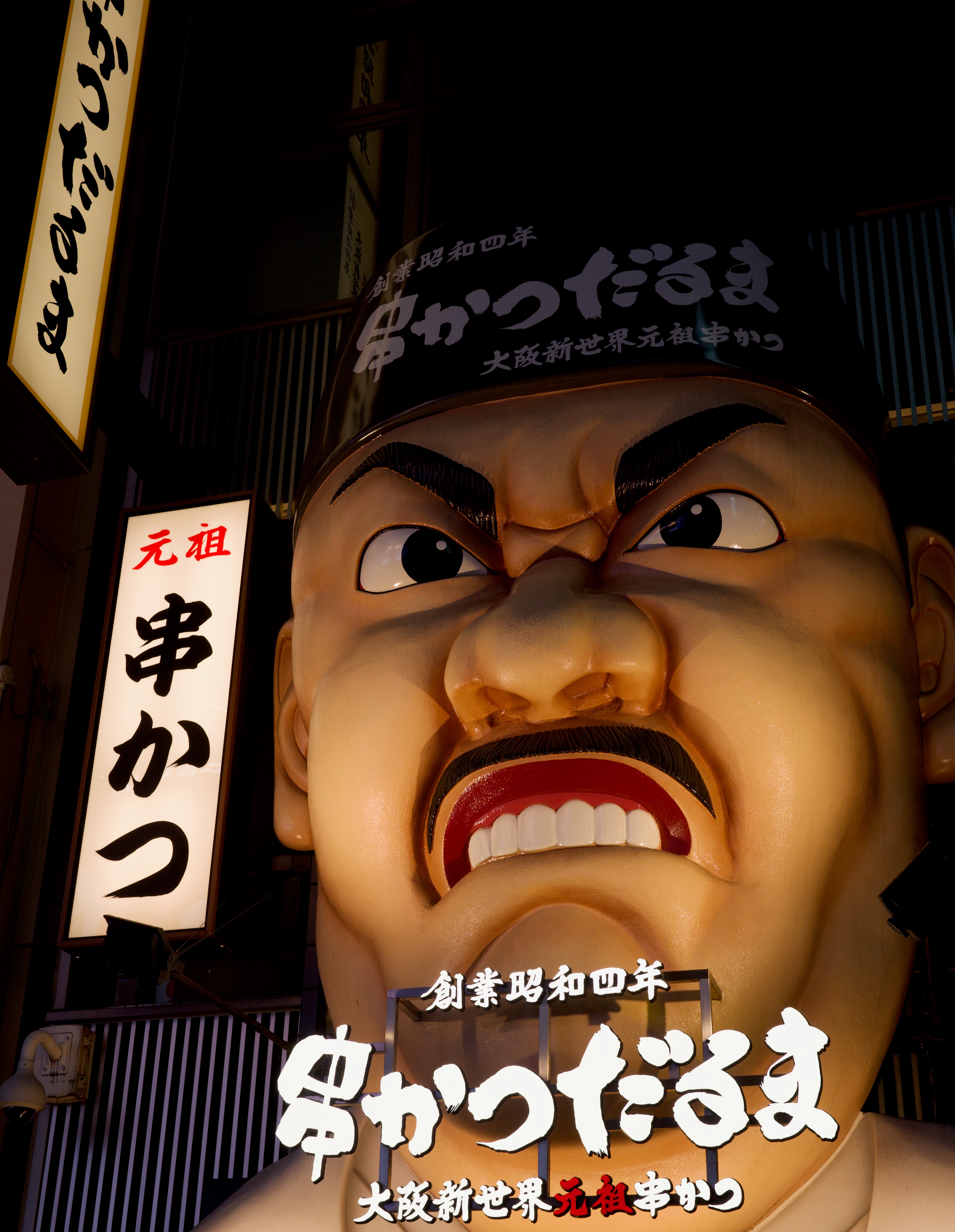A large illuminated theatrical face sign fills the street view.