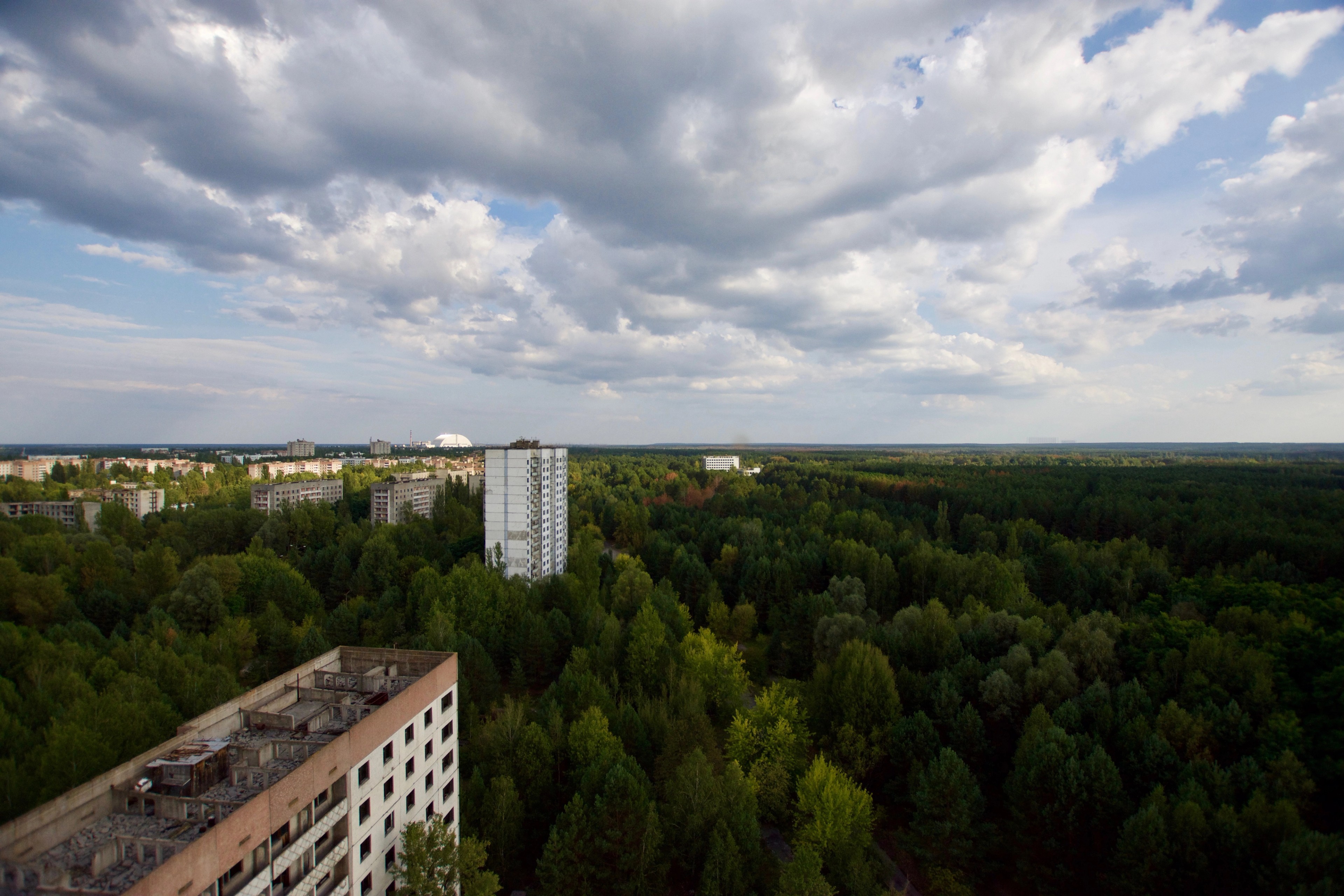 Aerial view of forest and disused buildings beneath cloudy skies.