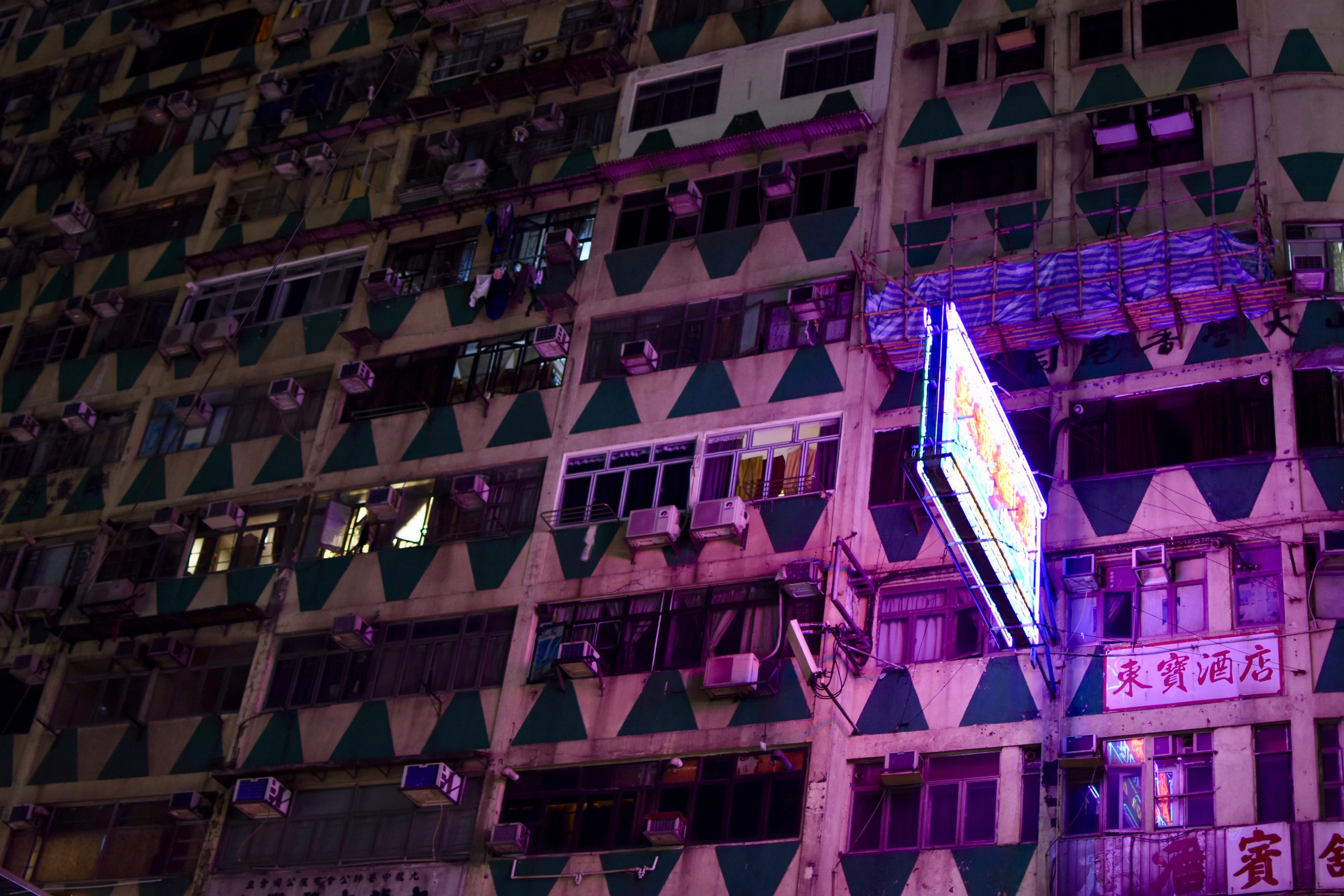 A triangular neon sign projects from a high-rise apartment block at night.