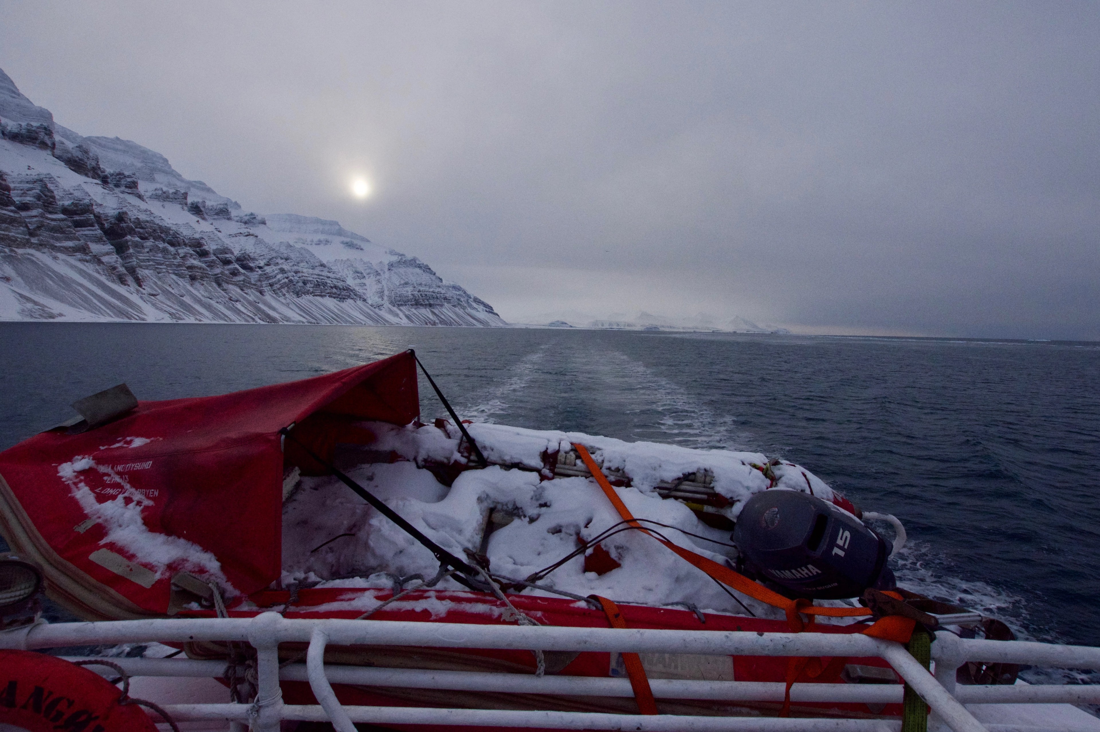 Red equipment is secured on the deck of a boat in icy water.