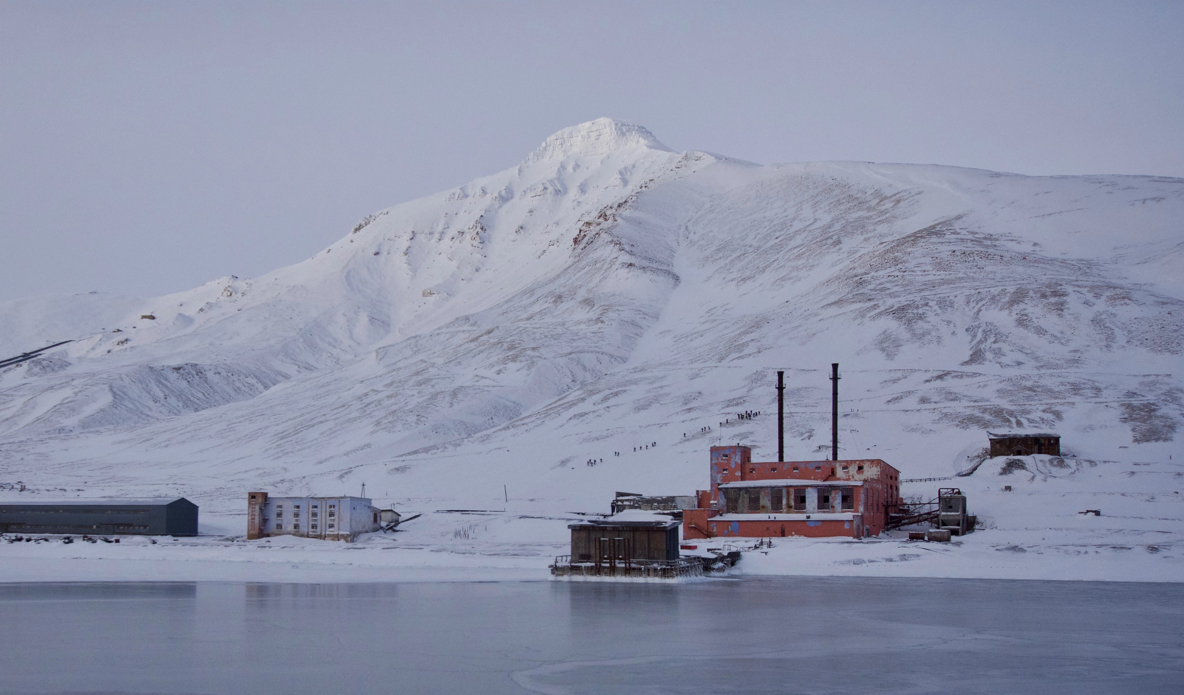 Industrial buildings stand beneath snowy mountains.