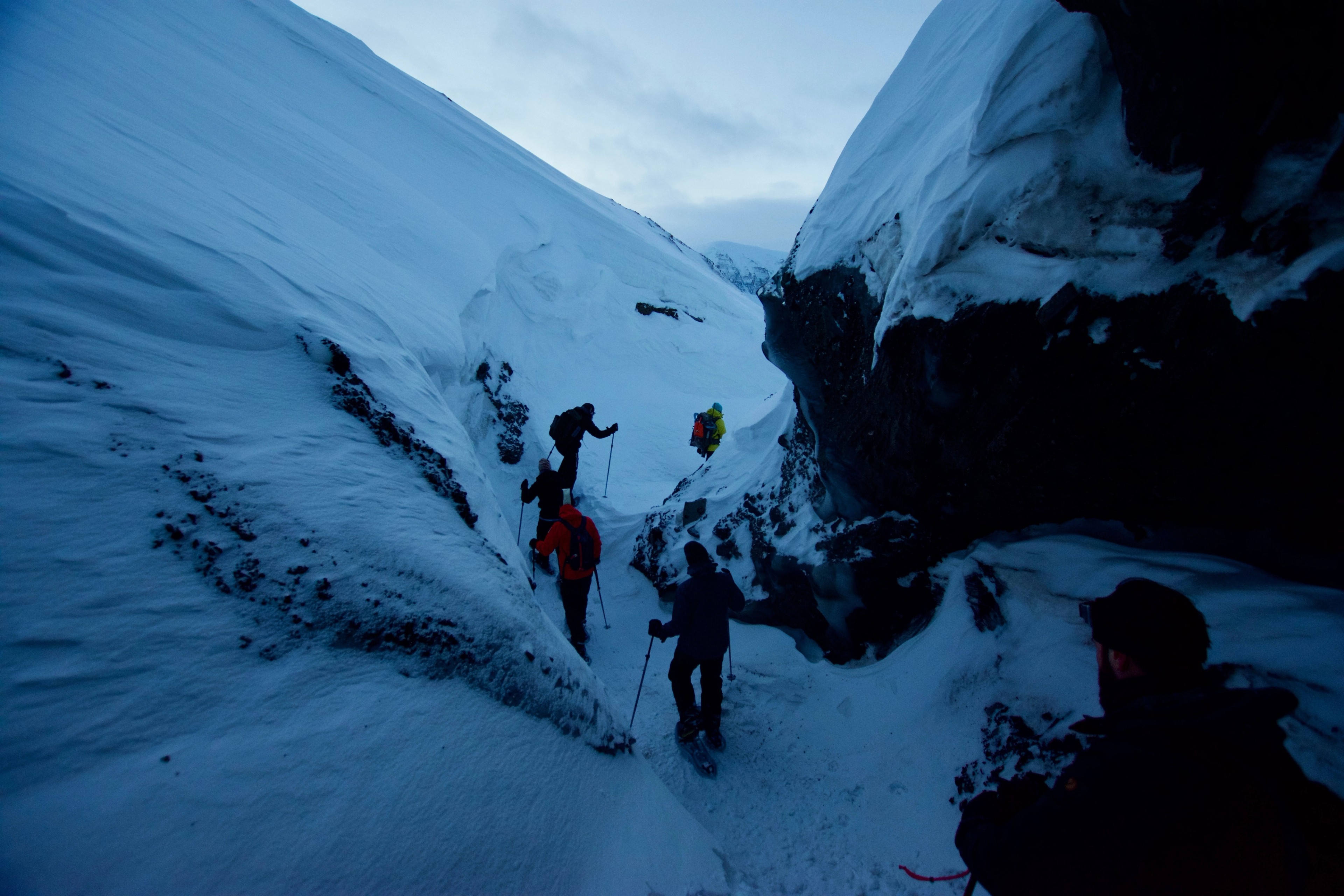 Hikers descend through a steep, shadowed ice ravine.