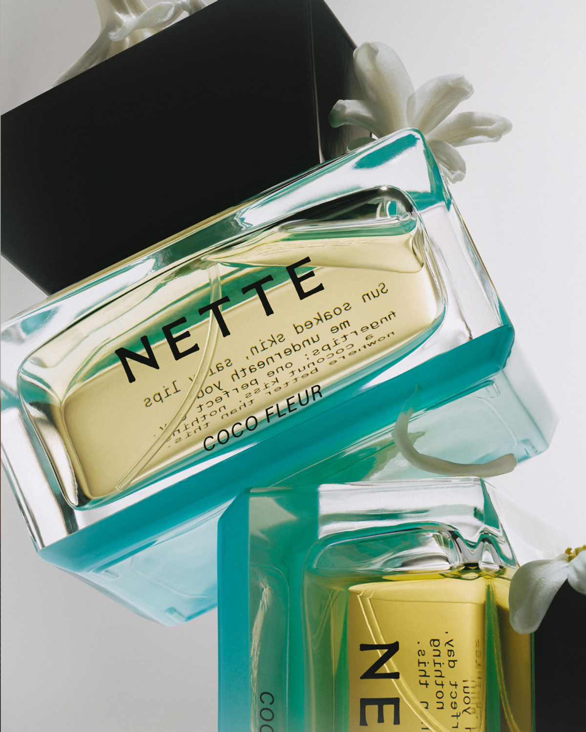 Two NETTE Coco Fleur perfume bottles with white flowers on white background