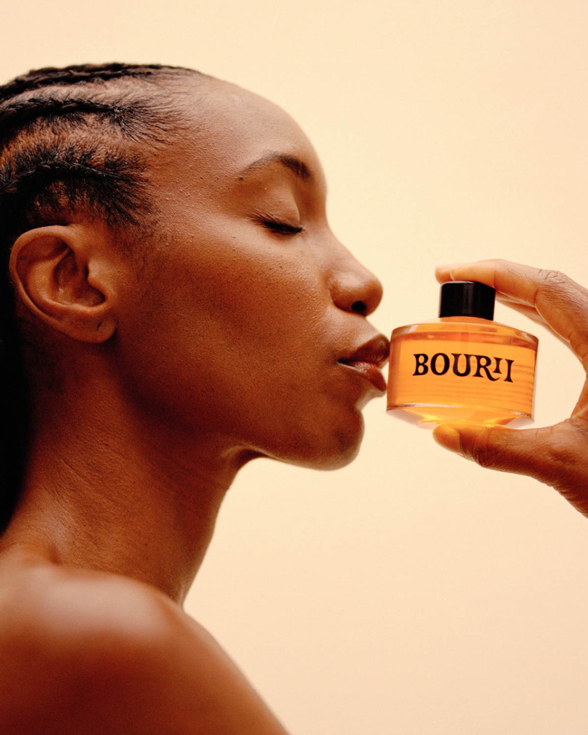 A woman with braided hair smiles while holding a bottle labeled "BOURI."
