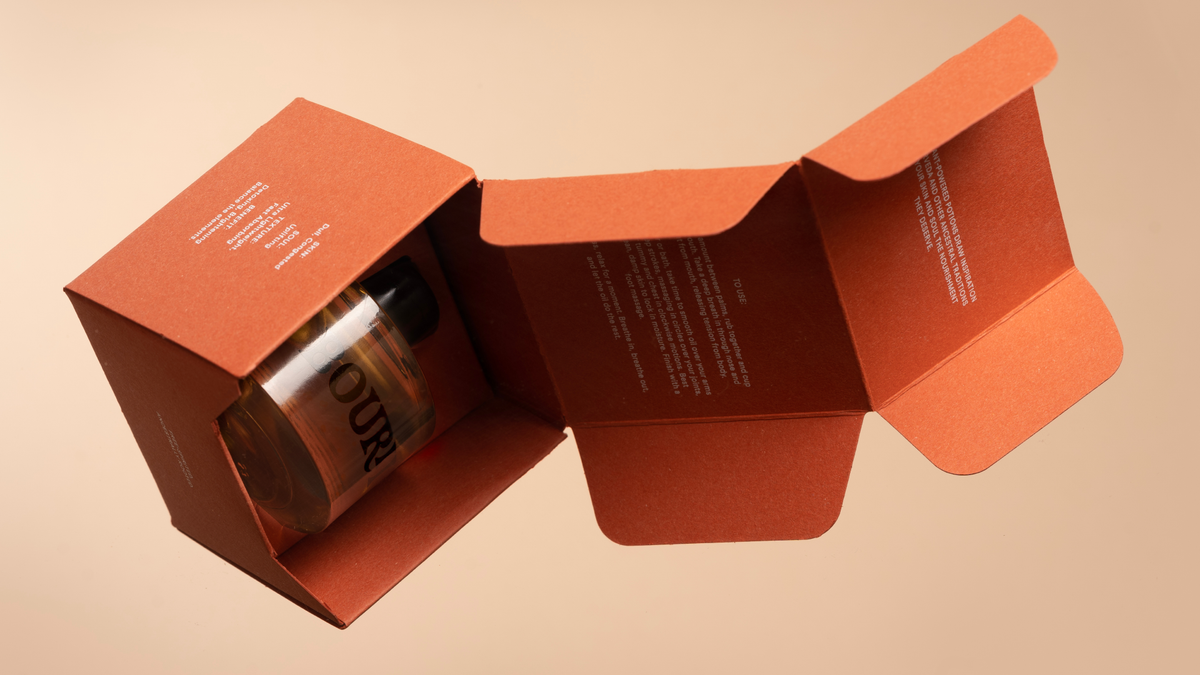 A dark amber-colored perfume bottle labeled "OUR" is displayed in an open, reddish-brown cardboard box. The box features text detailing usage instructions and certifications.