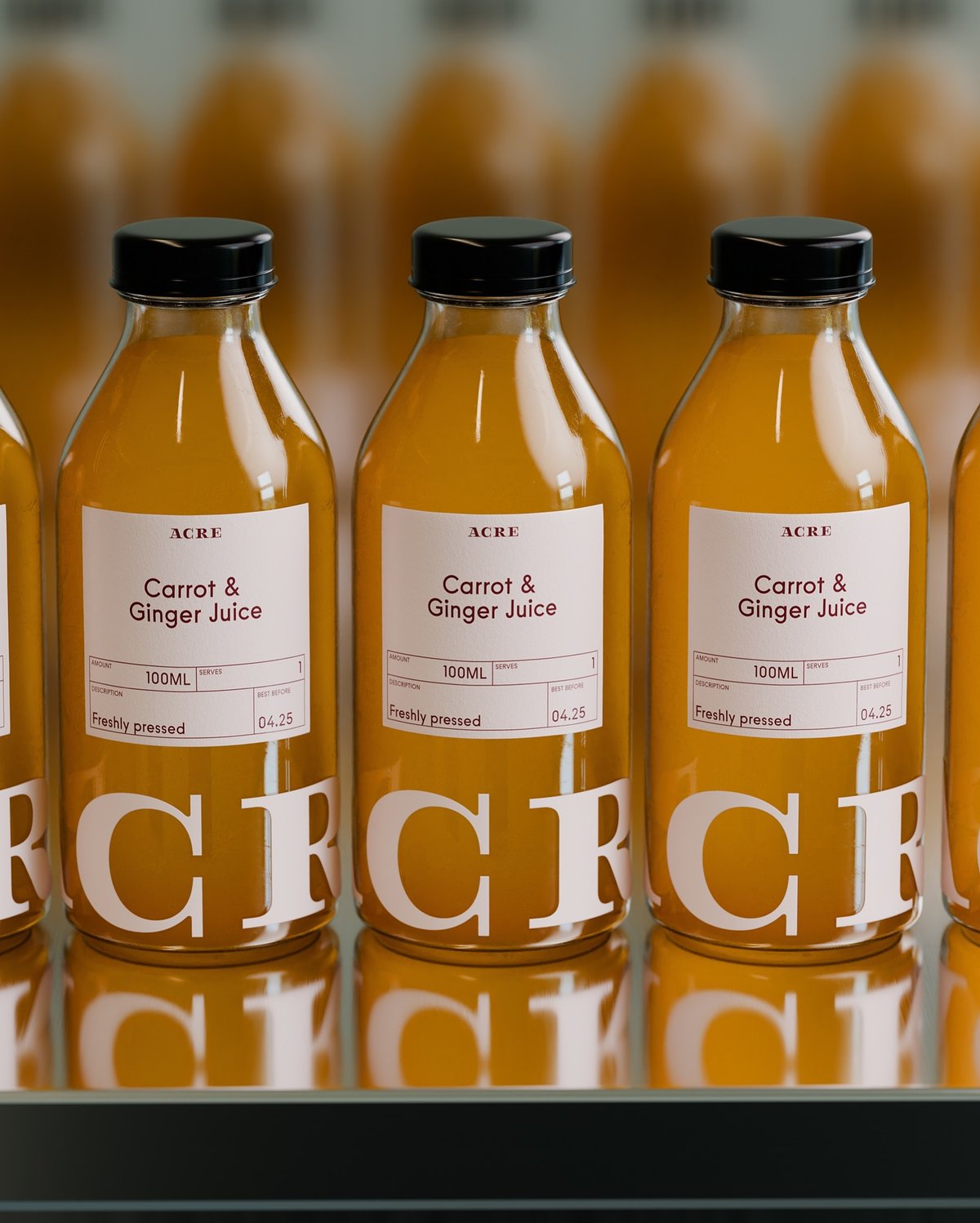 Four glass bottles of Acre Carrot & Ginger Juice, freshly pressed and labeled, are arranged on a reflective surface.