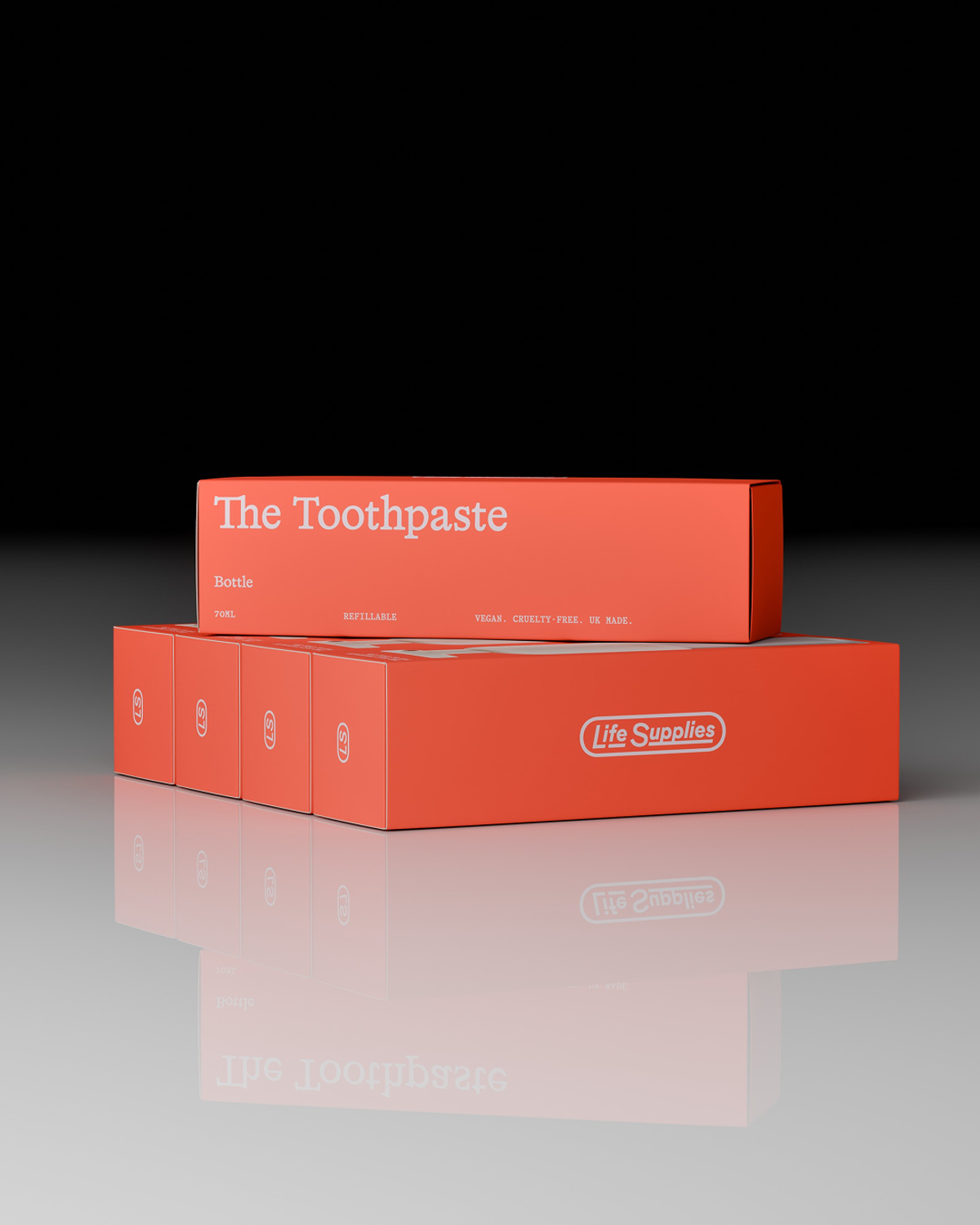 Two orange boxes of "The Toothpaste" product from Life Supplies are stacked on a reflective surface. The boxes are labeled as refillable and contain 70ml of toothpaste.