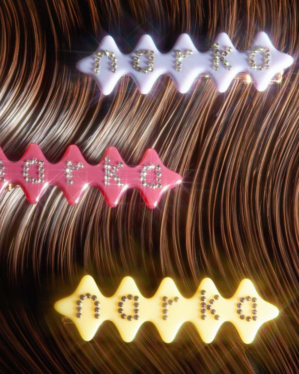 Three hair clips, each displaying the name "NARKA" in rhinestones, are arranged diagonally against a textured brown background.