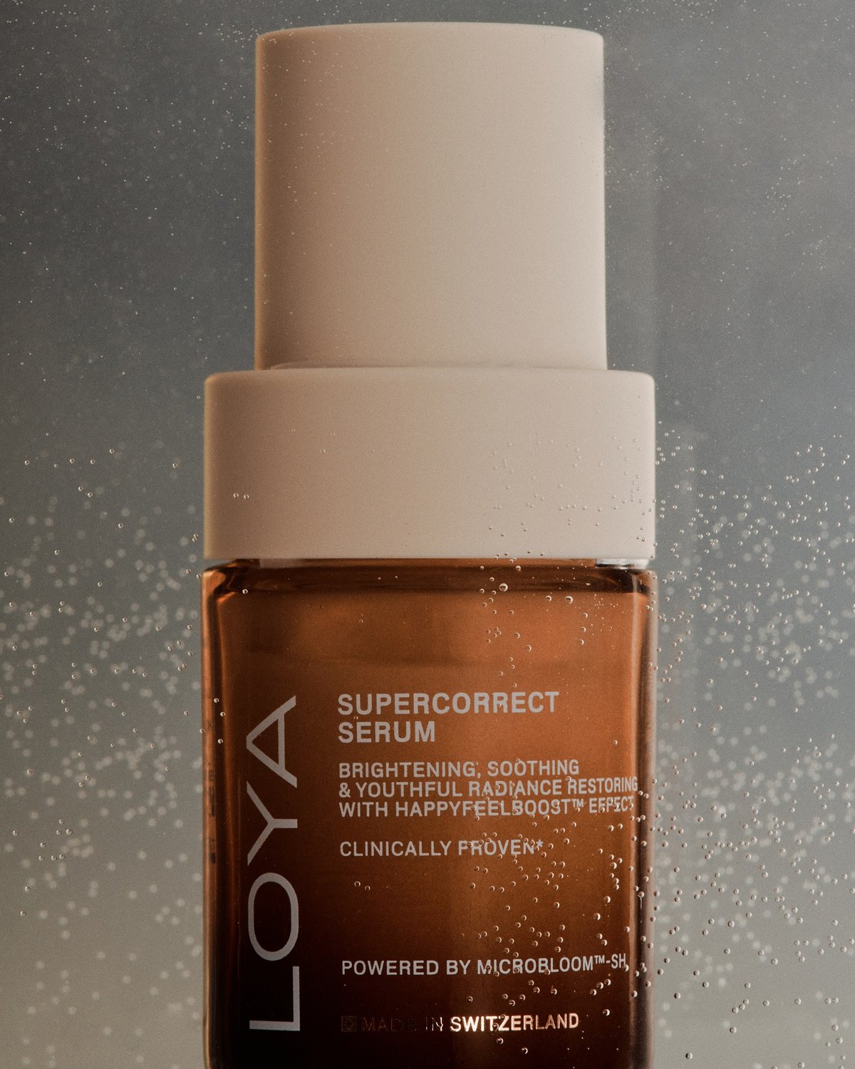 A bottle of Loya SuperCorrect Serum, a Clinically Proven product from Switzerland, is shown against a textured background. The brown bottle features white text and a light-colored cap.