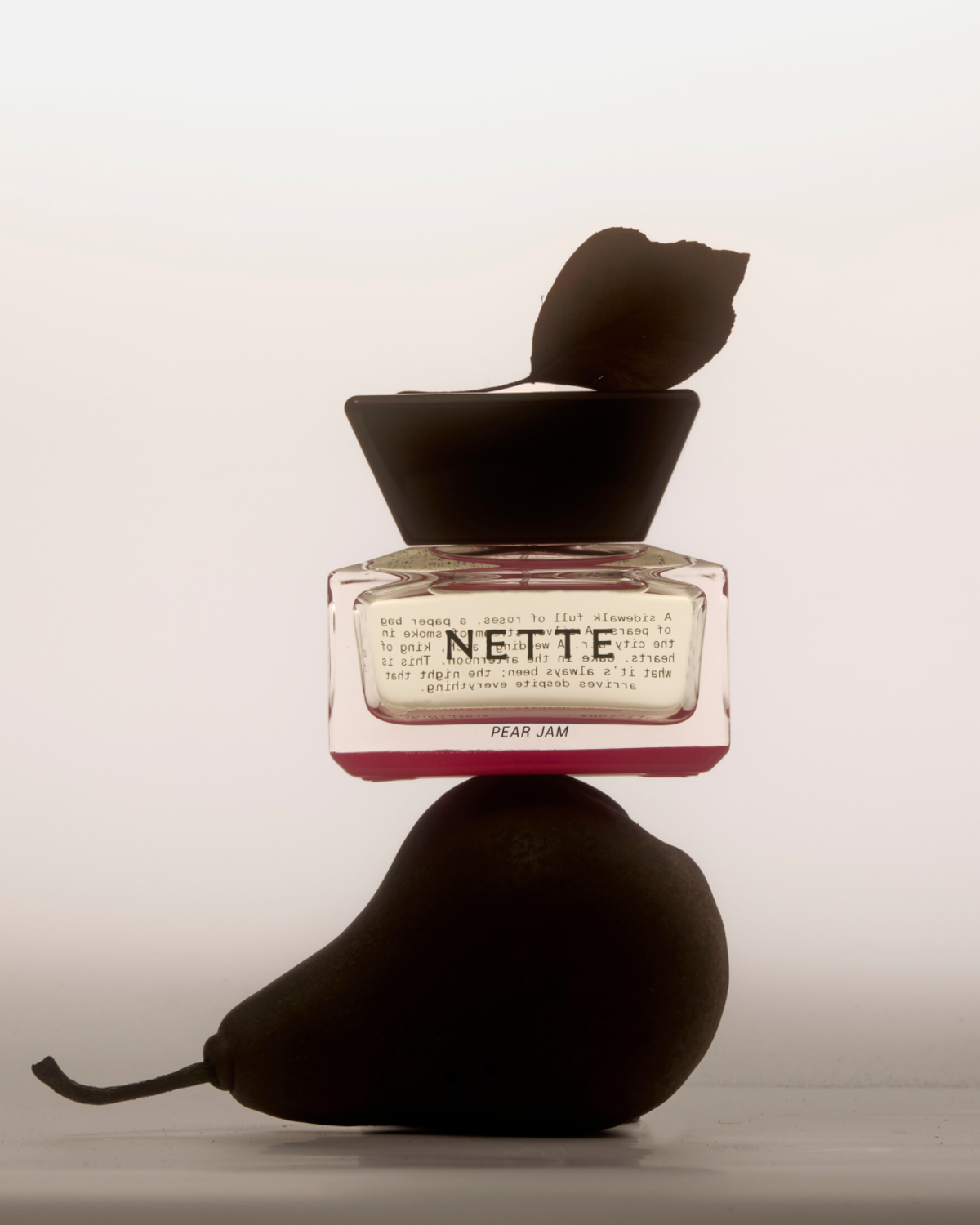 NETTE Pear Jam perfume bottle balanced atop two dark pears
