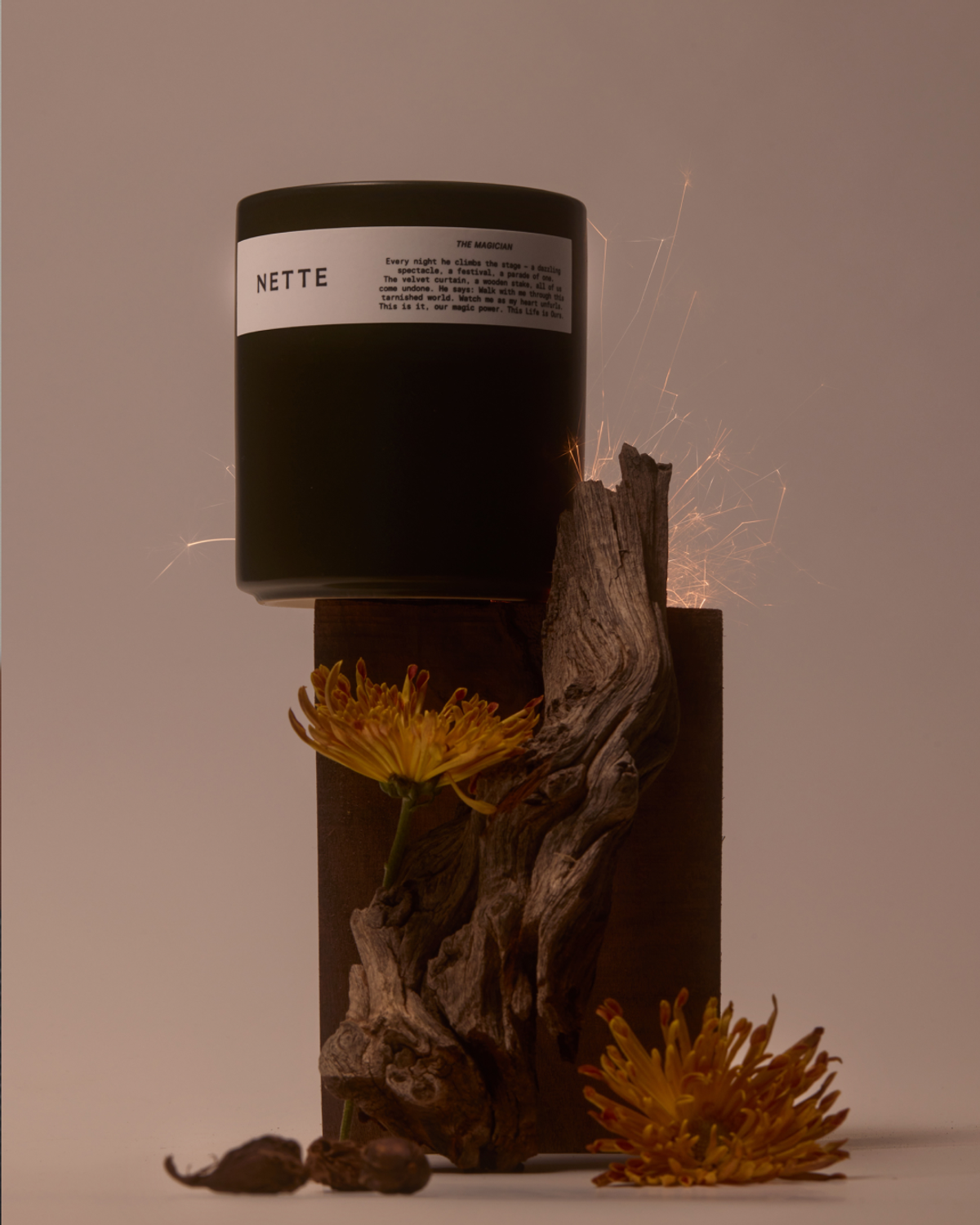 Black NETTE candle on wooden base with dried flowers and sparks