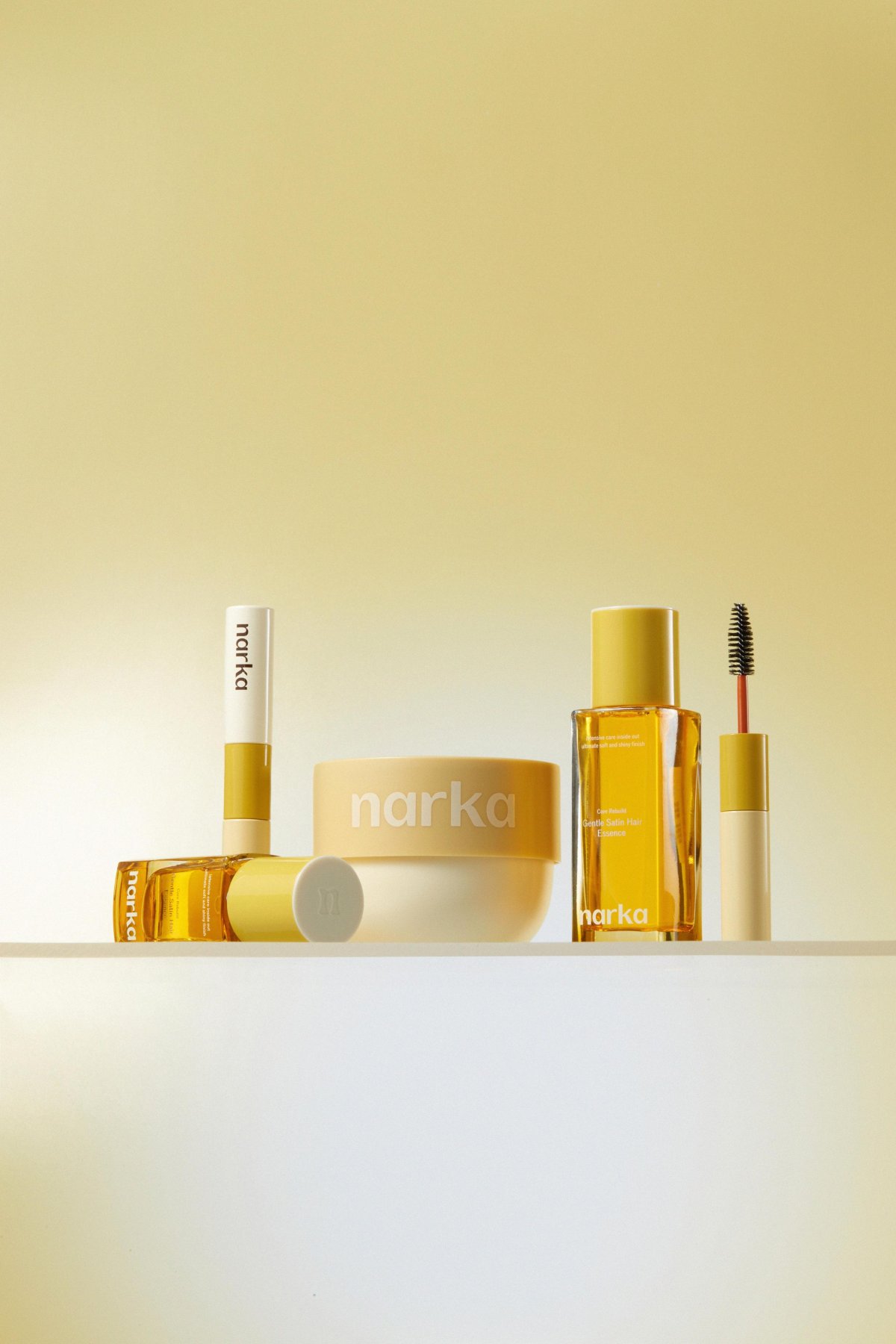 Narka makeup products, including a cream, lipstick, mascara, eye shadow, and eyeliner, are displayed on a white surface against a gold background.
