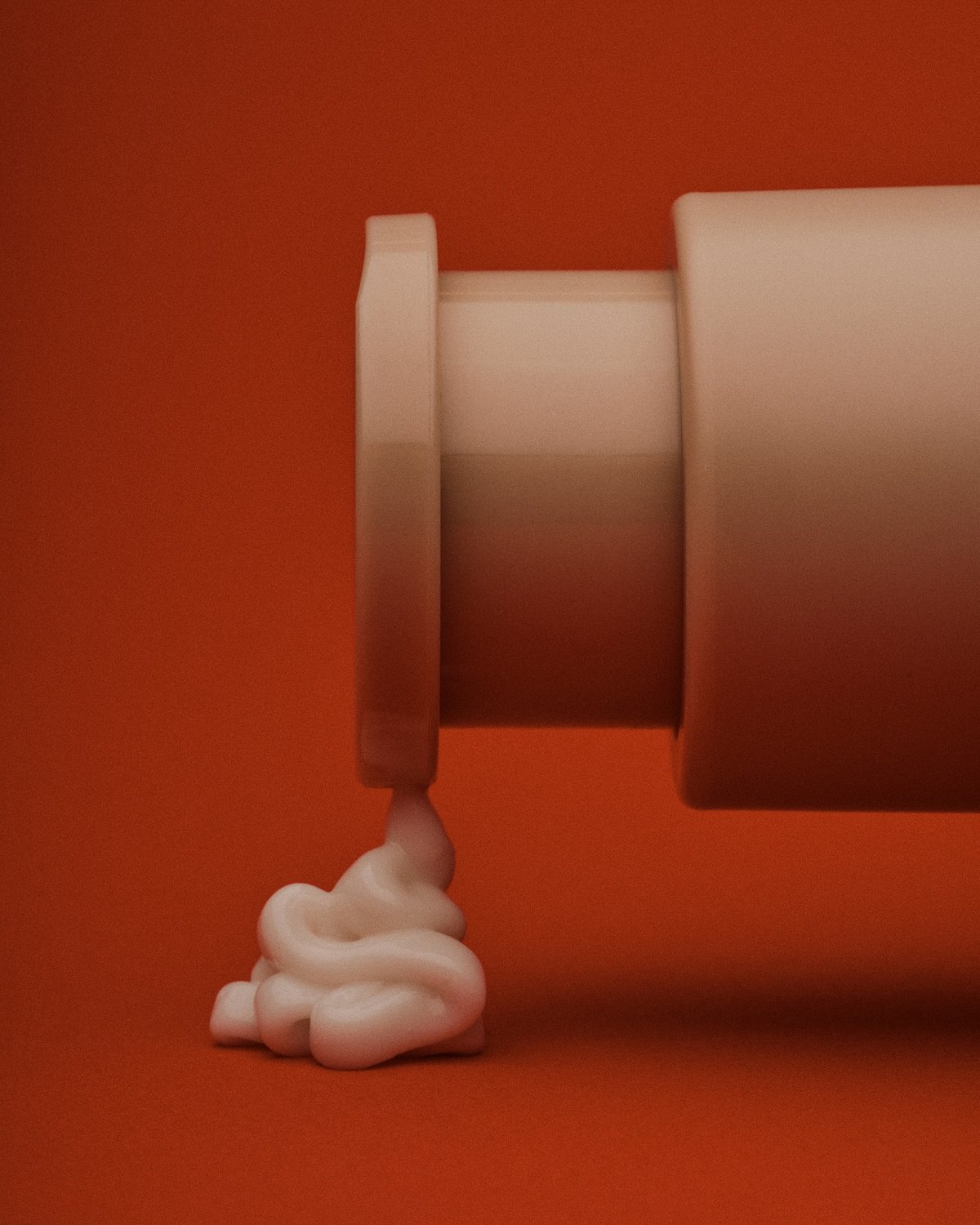 A light beige tube of cream spills onto a red background. The cream is unevenly distributed, resembling a splash.