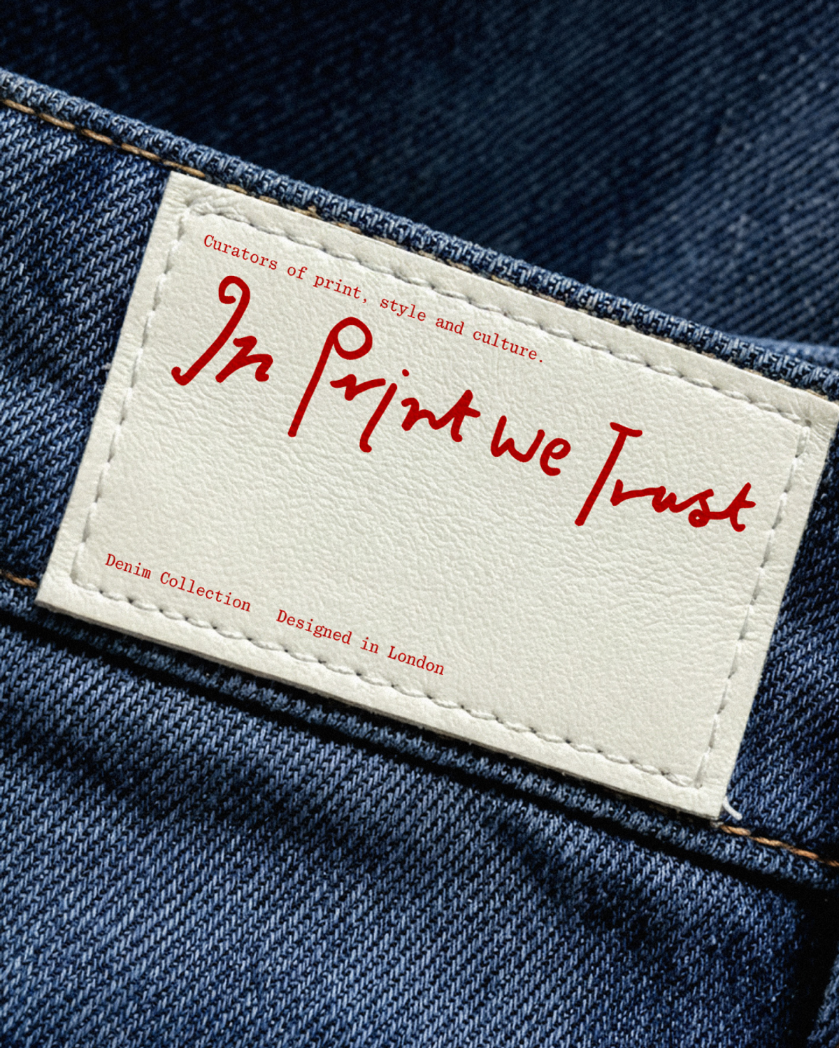 A white label on a pair of blue denim jeans reads "In Print We Trust," "Curators of print, style and culture," "Denim Collection," and "Designed in London."