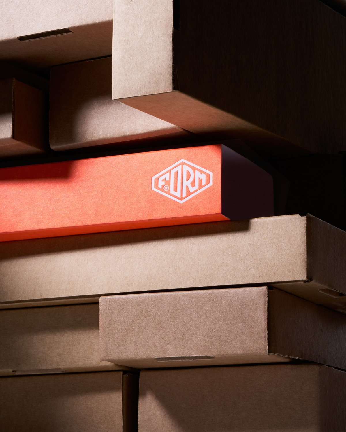 A stack of cardboard boxes, primarily light brown, features an orange rectangular box with the "FORM" logo.