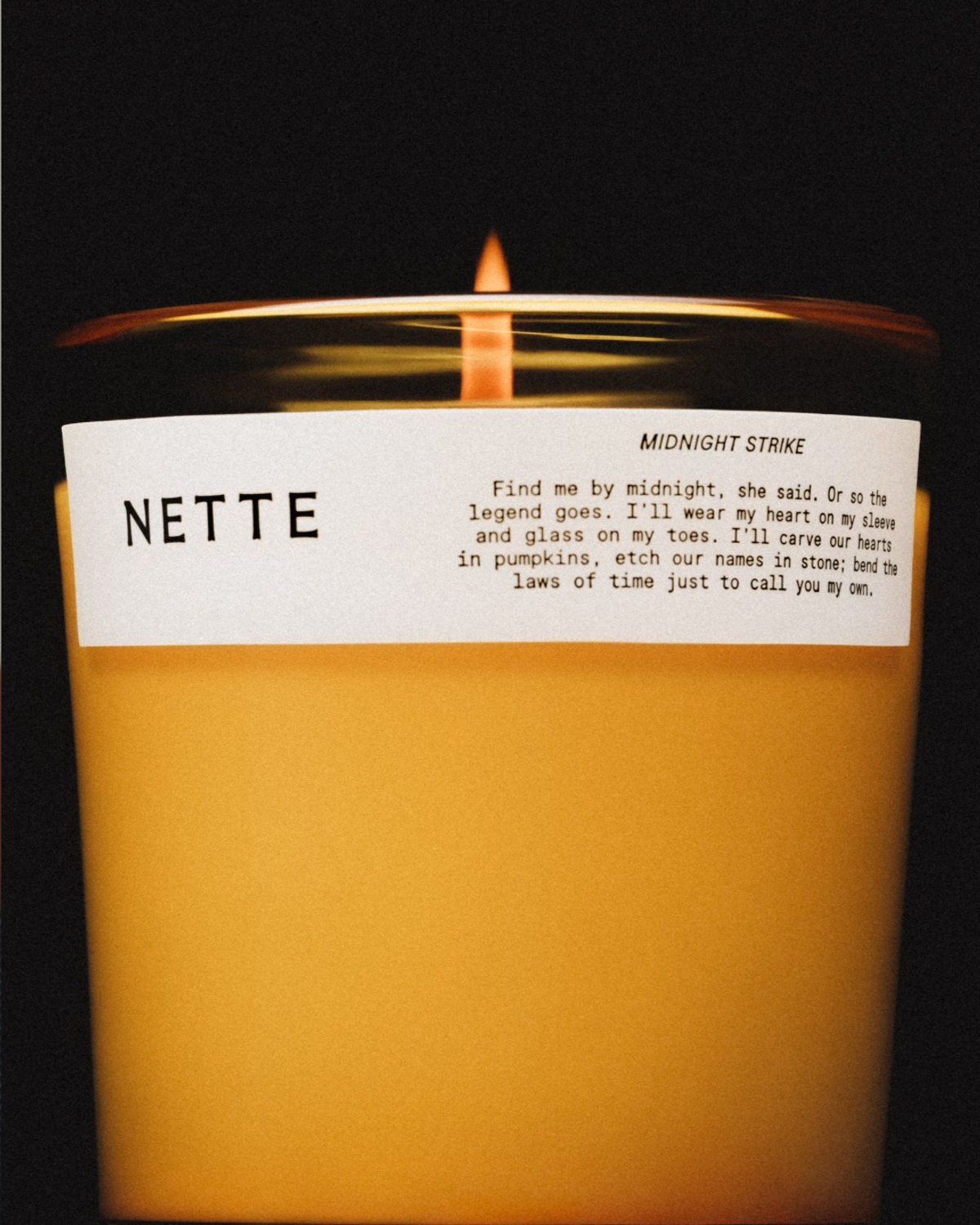 Lit NETTE Midnight Strike candle in glass holder with white label