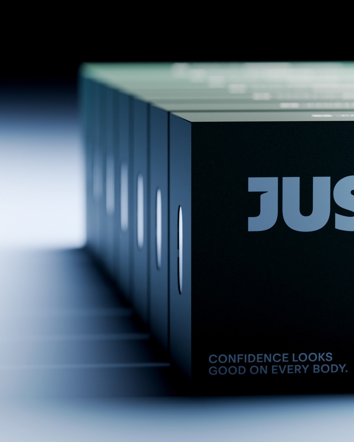 A row of dark-colored boxes with cutouts displays the "JUS" logo and the phrase "CONFIDENCE LOOKS GOOD ON EVERY BODY."