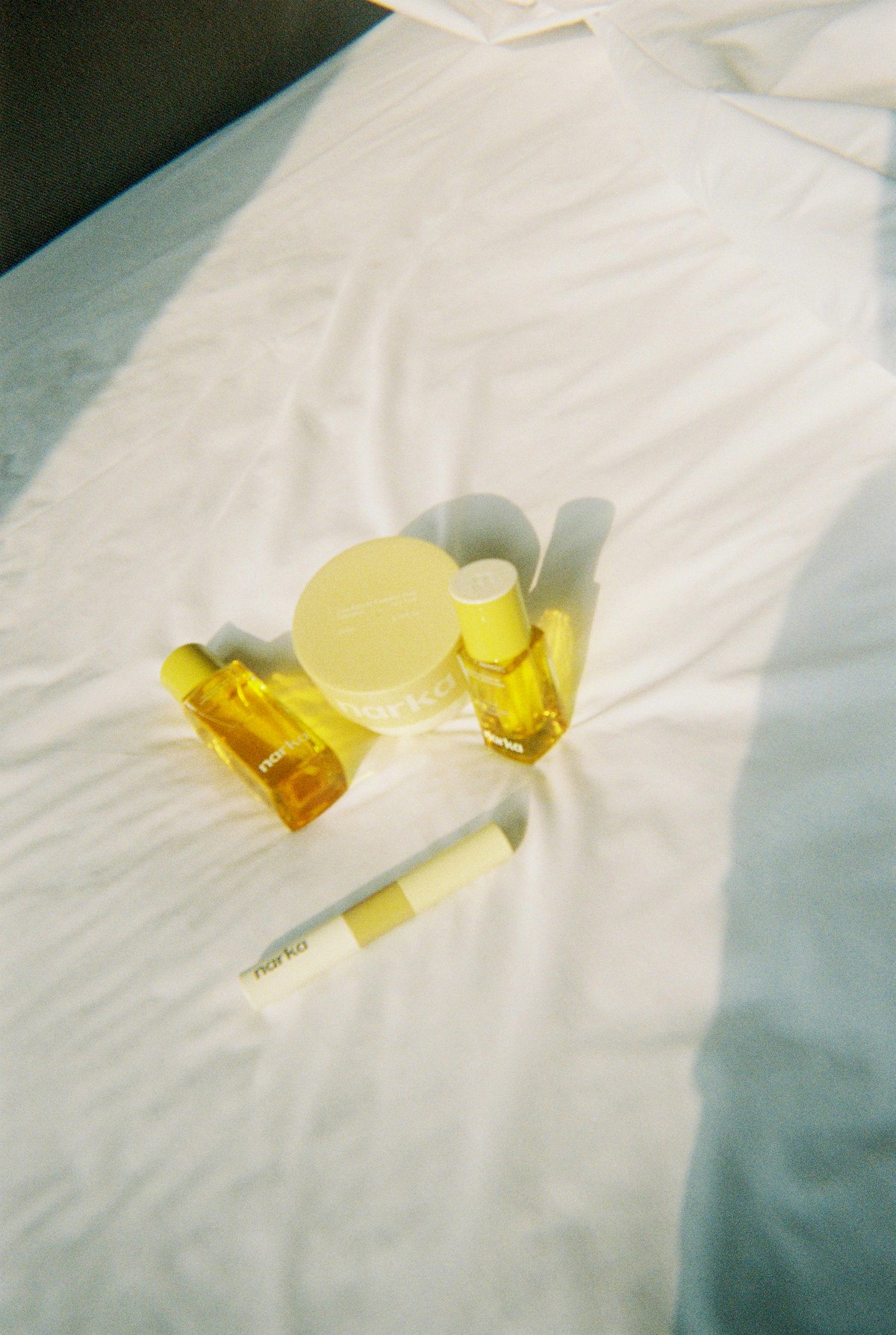 Narka skincare products, including bottles, a jar, and a tube, are arranged on a white bedspread.