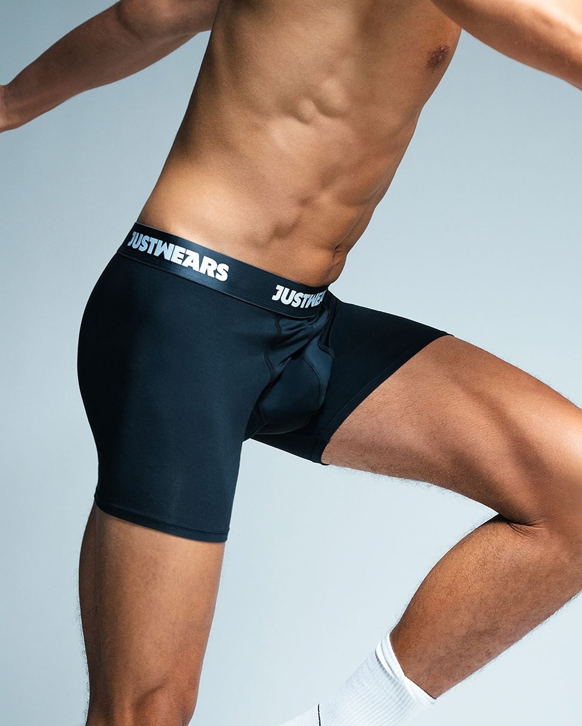A person wearing black JustWears boxer briefs is shown mid-stride against a light gray background.