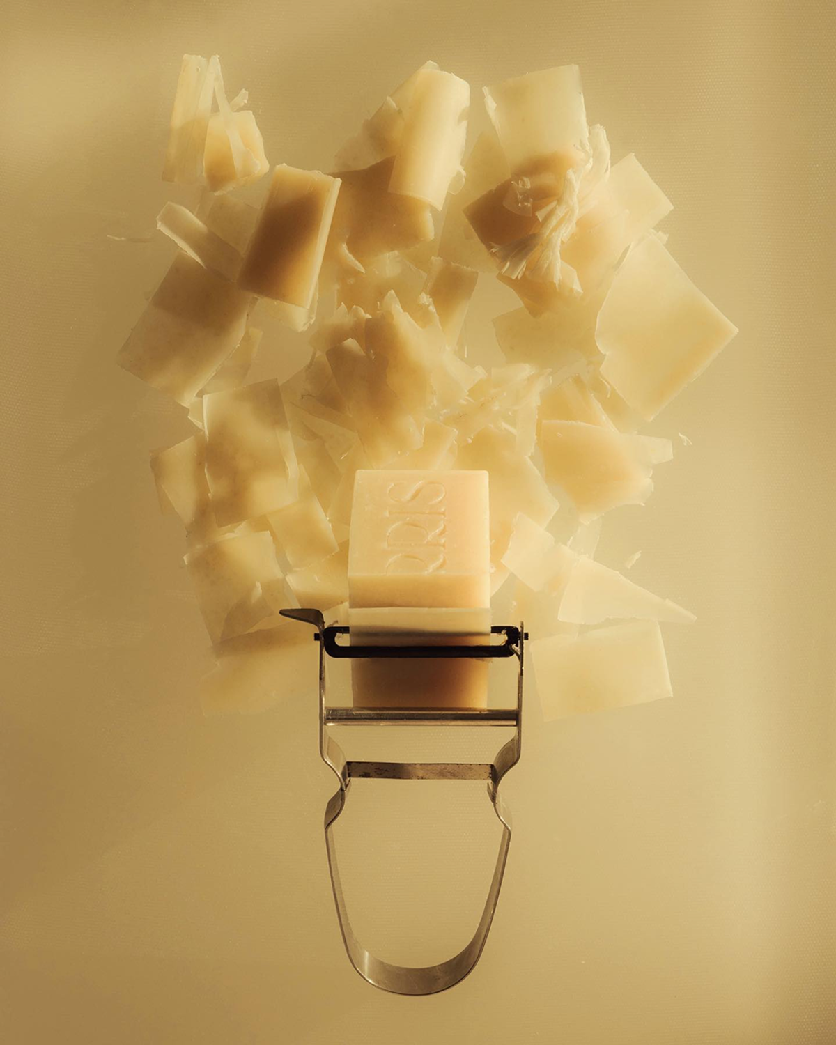 A bar of soap, cut into irregular pieces, rests on a metal peeler against a light background.