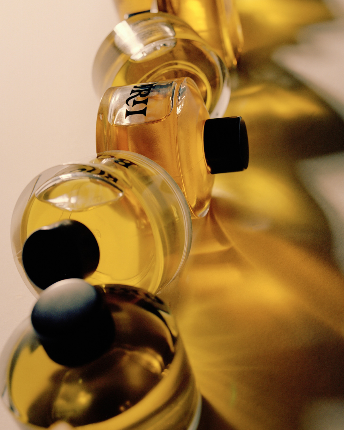 Several amber-colored perfume bottles with black caps are arranged diagonally, casting shadows on a light background. The bottles are labeled with partially visible text.