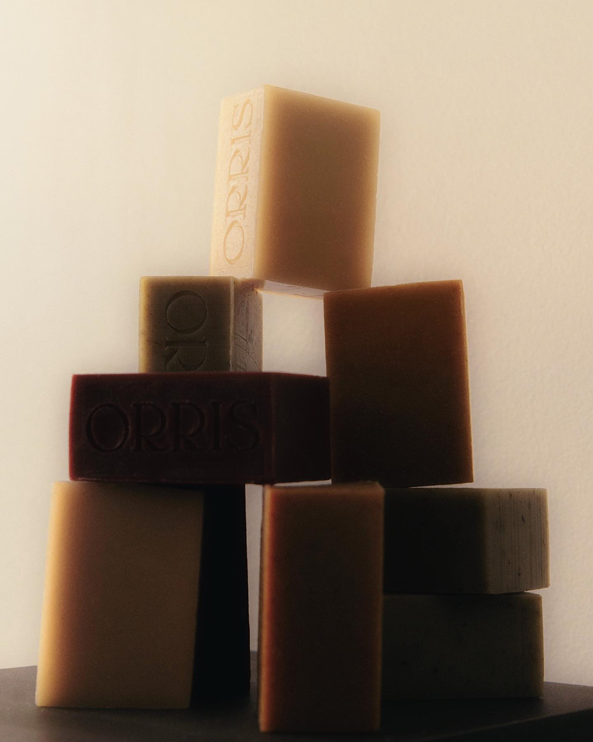 A pyramid of rectangular bars of varying colors and textures, labeled "ORRIS," sits on a dark surface against a light background.