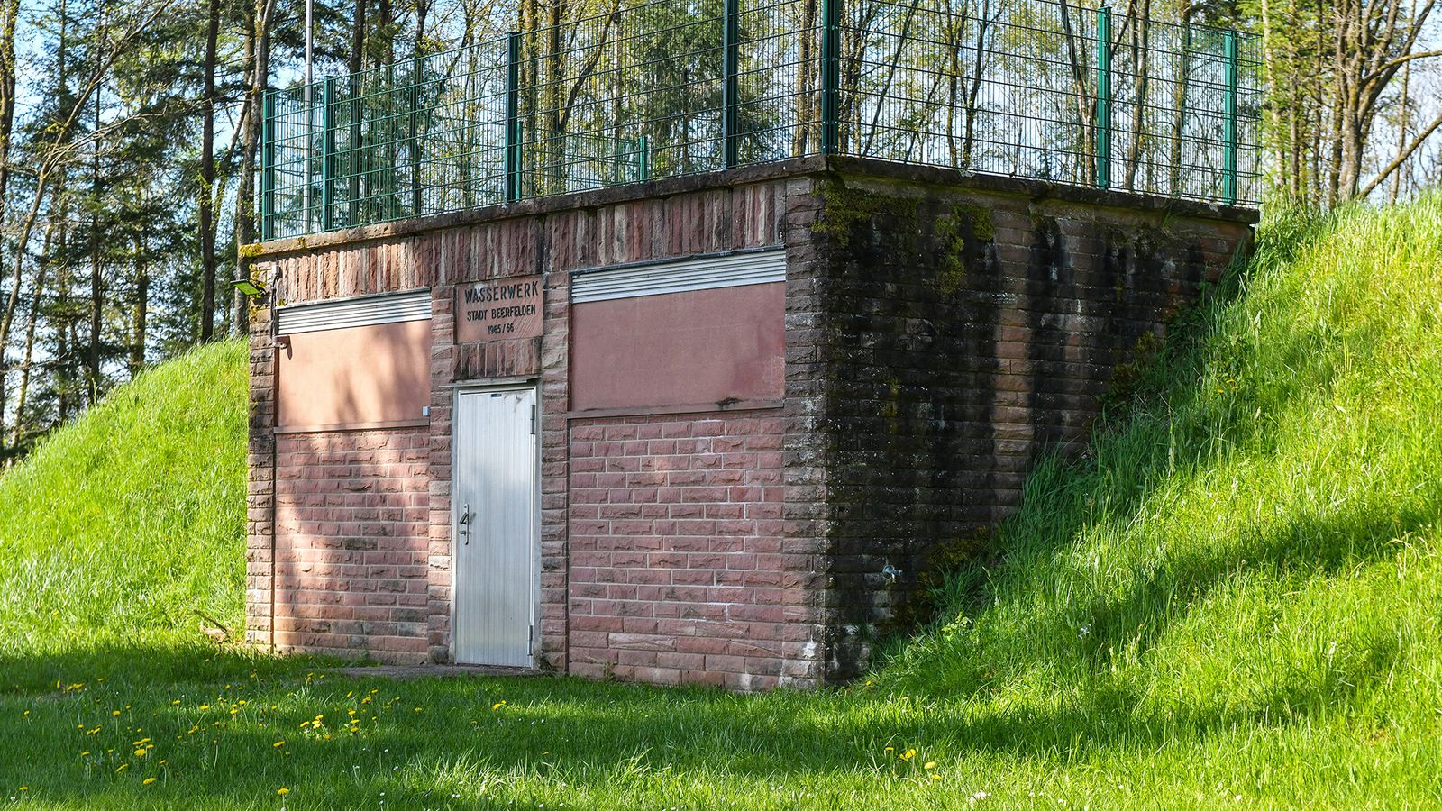 Altes kommunales Wasserwerk-Schieberhaus mit Erdwall in grüner Umgebung