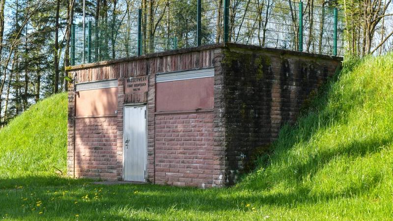 Old municipal water works valve house with earthen embankment in green surroundings