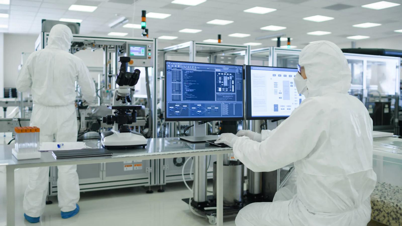 Pharmamitarbeiter in Reinraum-Schutzanzügen arbeiten an Produktionsanlage mit MES-Dashboard