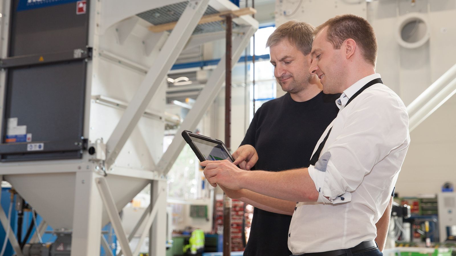 Two technicians checking filter system monitoring on tablet in front of industrial filter housing