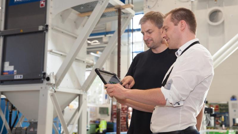 Zwei Techniker prüfen Filteranlage-Monitoring auf Tablet vor industriellem Filtergehäuse