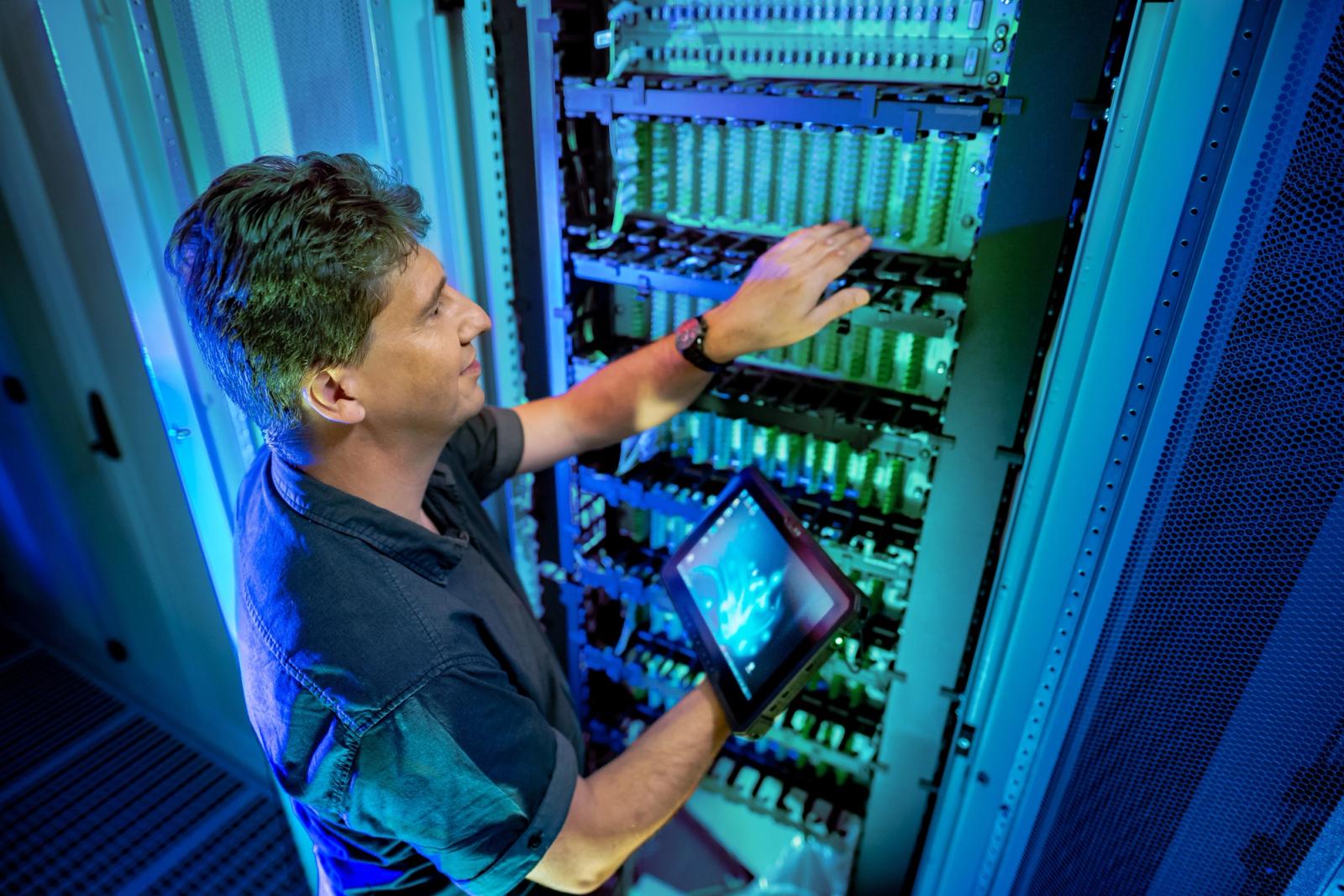 IT-Techniker mit Tablet inspiziert blaues Server-Rack im Rechenzentrum