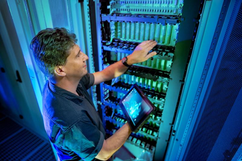 IT-Techniker mit Tablet inspiziert blaues Server-Rack im Rechenzentrum