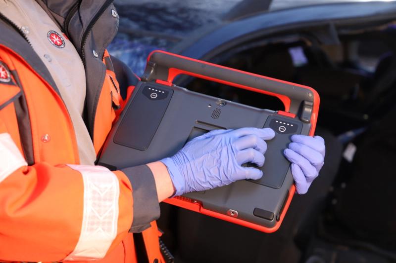 Malteser-Sanitäter hält robustes IoT-Notfalltablet in Schutzhandschuhen