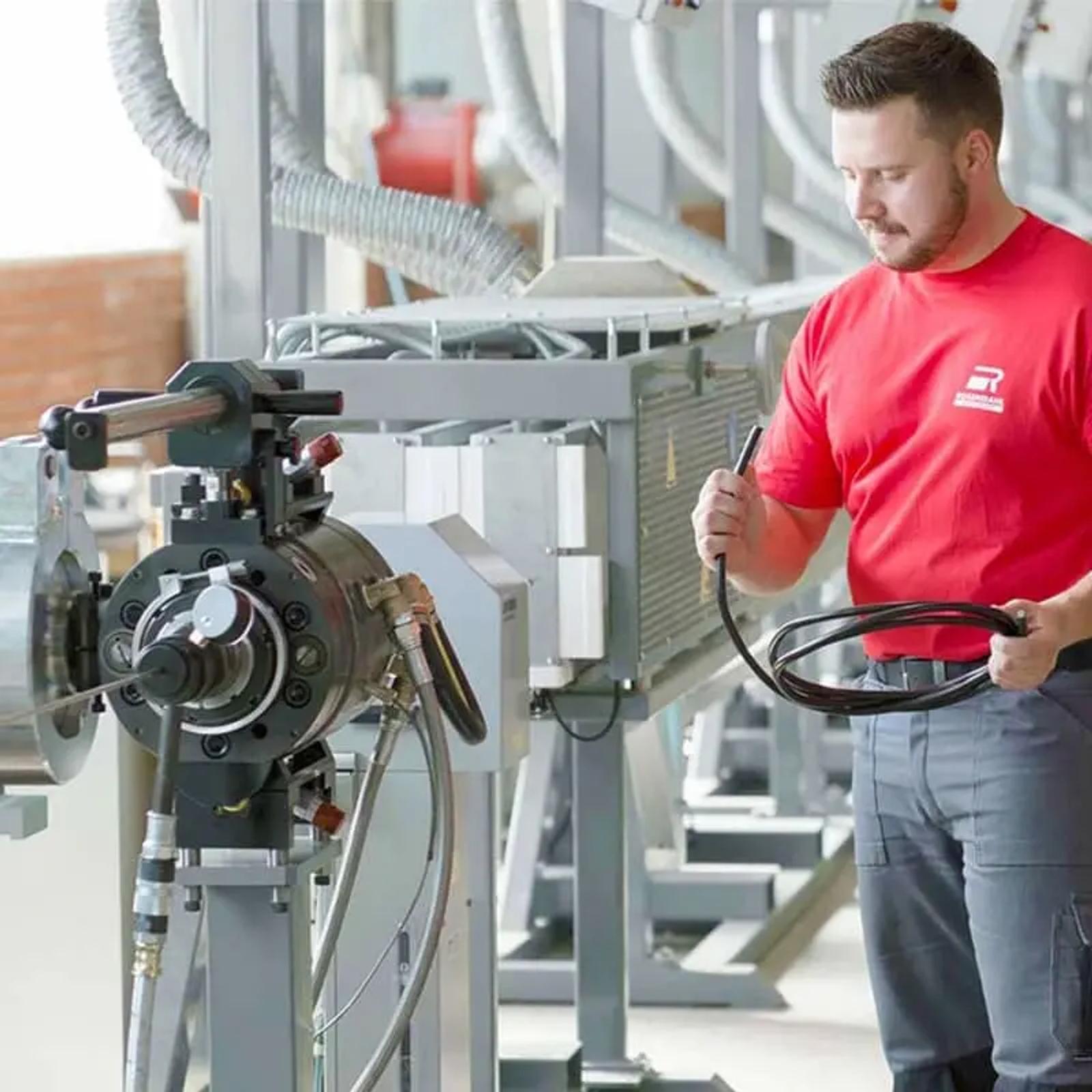 Rosendahl Techniker hält fertiges Kabel neben Extrusionskopf der Fertigungsanlage