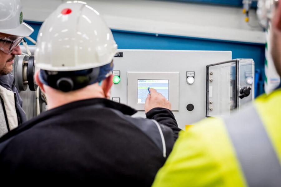 Techniker mit Schutzhelm bedient das Touch-Bedienpanel einer AQUACHEM-Filterpresse