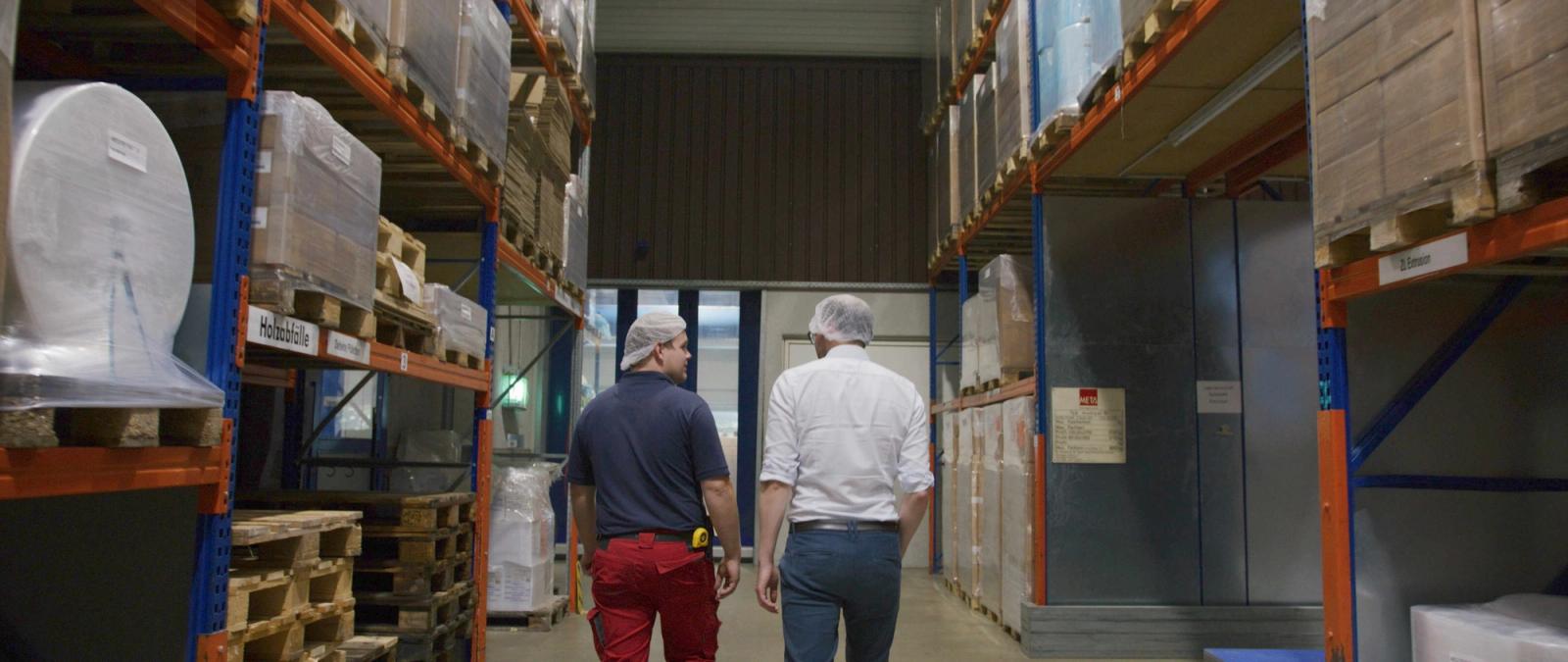 mk Plast Mitarbeiter gehen durch Materiallagerhalle mit Regal-Systemen