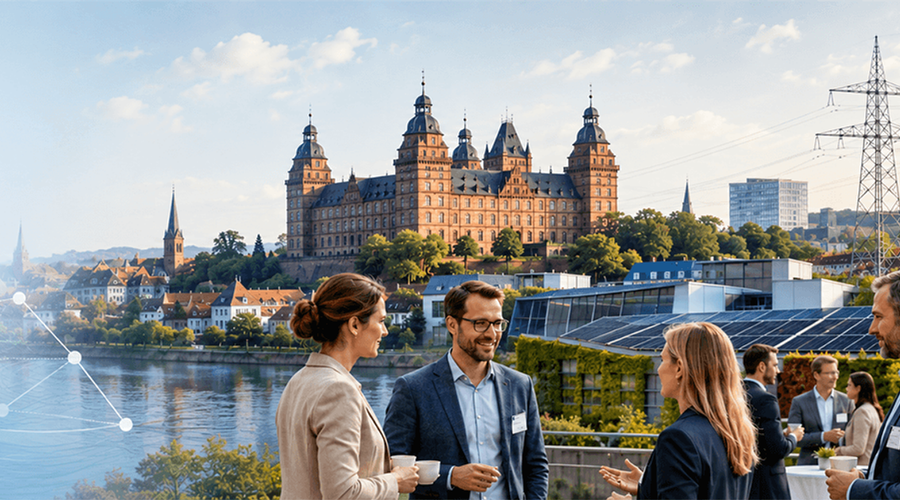 Johannisburg Palace above the river Main in Aschaffenburg, with three forum attendees talking in the foreground next to a building with a rooftop solar array and a green facade.