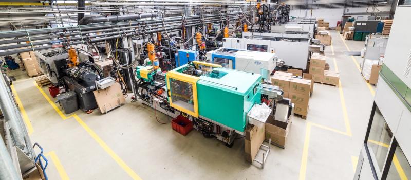 Spritzgusstechnik-Produktionshalle von oben mit Spritzgussmaschinen und Roboterarmen