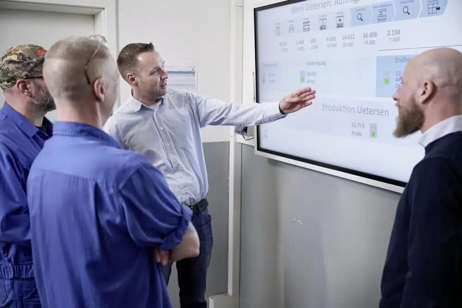 Mitarbeiter erläutert Produktionsdaten auf Peakboard-Monitor im Eingangsbereich