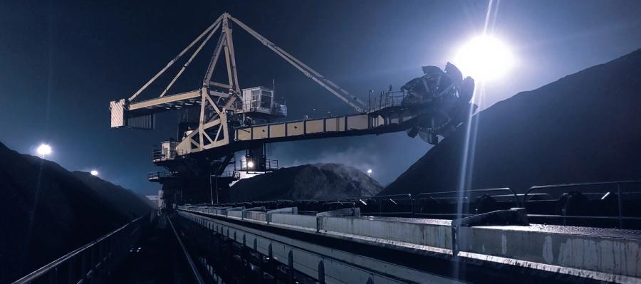 Schaufelradgerät an einer Schüttgut-Halde bei Nacht mit langem Förderband im Vordergrund