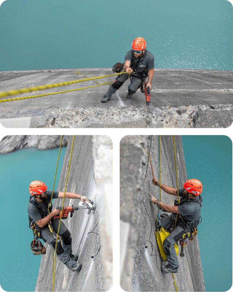 Industriekletterer mit orangem Helm am Seil an der Staumauer Limmernsee: Er bohrt Halterungen in den Beton und verlegt Sensorkabel, darunter der türkisfarbene Stausee