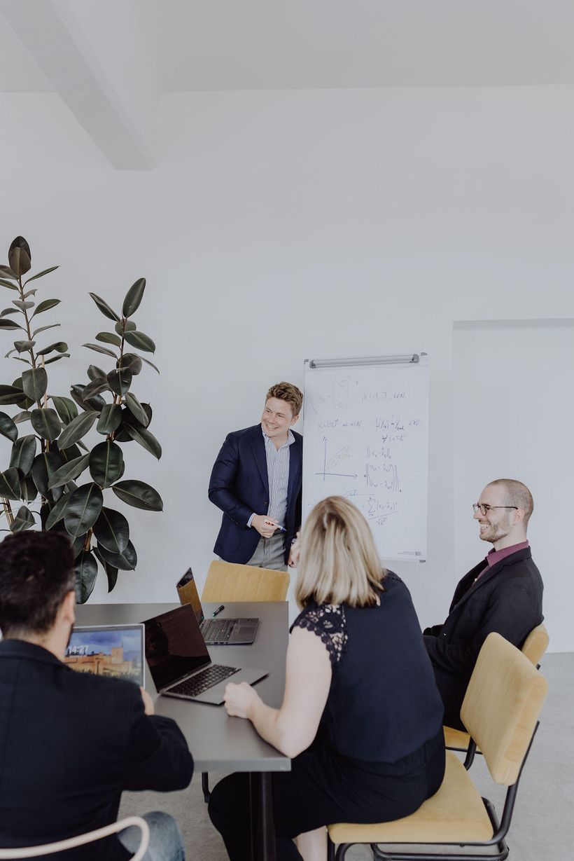 Teammeeting mit Whiteboard-Präsentation und Laptops für Produktionsoptimierung