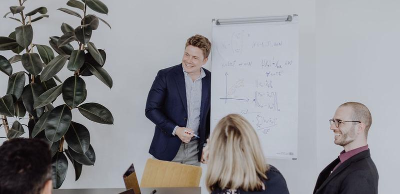 Teammeeting mit Whiteboard-Präsentation und Laptops für Produktionsoptimierung