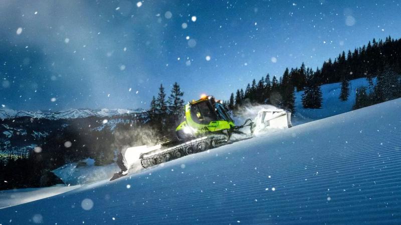 Snow groomer at night on ski resort slope during snowfall